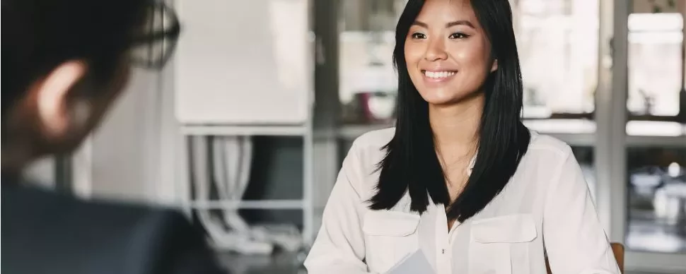 Woman smiling during a meeting, seated at a desk with documents.