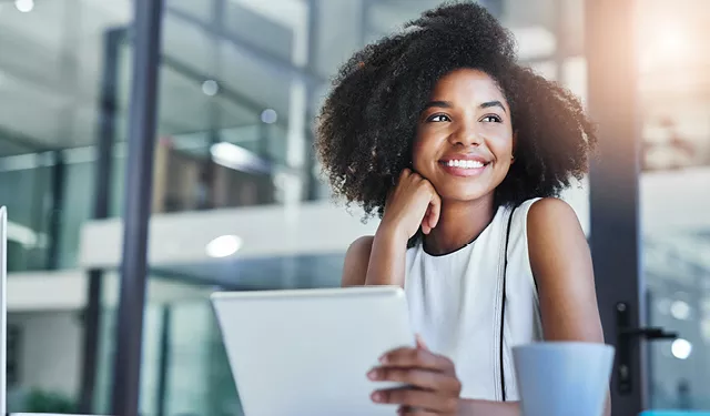 Smiling woman with curly hair holding a tablet in a modern office.