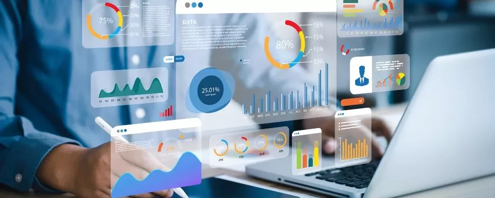 Person analyzing data visualizations on a laptop with graphs and charts displayed on a transparent screen.