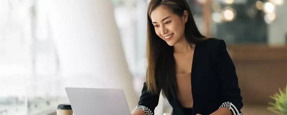 Woman smiling while using a laptop in a cafe.