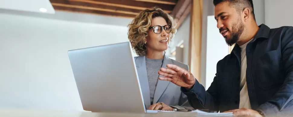 Two people discussing work at a desk with a laptop.