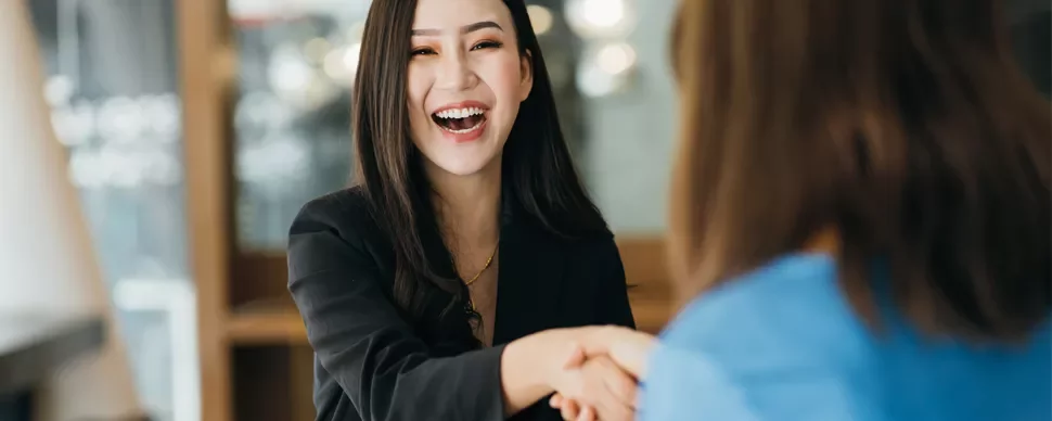 Woman in a black blazer smiling and shaking hands with another person.