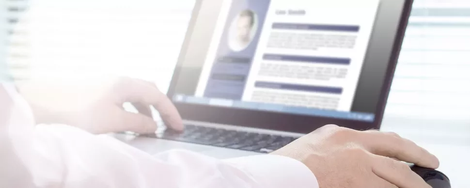 Person reviewing a resume on a laptop screen, hands resting on the keyboard.