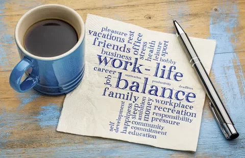 Coffee cup and pen on a table with a napkin featuring a word cloud about work-life balance.
