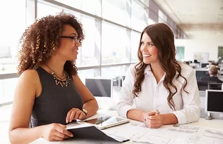 Two women smiling and talking in a bright office setting.