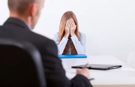 Woman sitting at a table with her head in her hands, looking stressed.