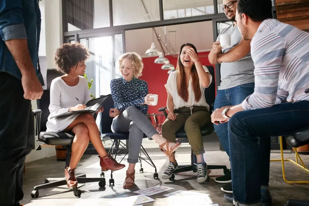 Group of colleagues laughing and chatting in an office setting.