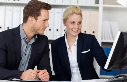 Two professionals in an office discussing a project at a computer.