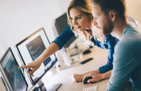 Two people collaborating on computer screens displaying code.