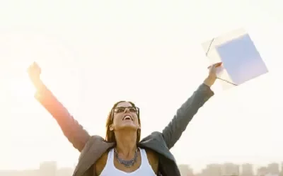 Person stands joyfully with arms raised, holding a folder against a bright sky.