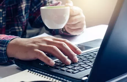 Person typing on a laptop while holding a coffee cup.