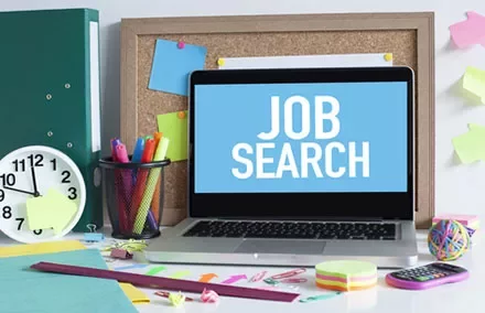 Laptop screen displaying 'Job Search' beside colorful office supplies.
