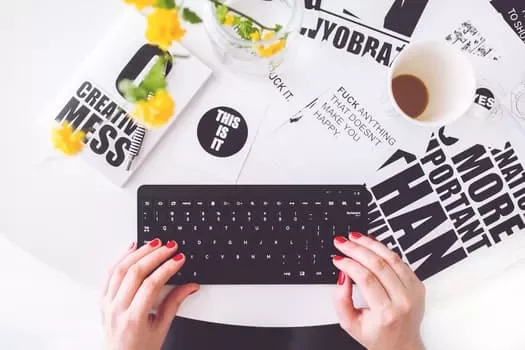 Hands typing on a keyboard with motivational posters and a coffee cup on a white table.