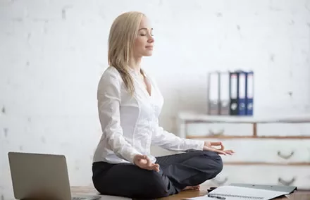 Woman meditating on desk in office attire.
