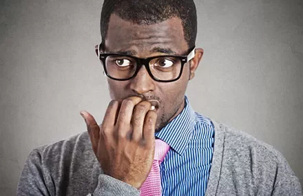 Man with glasses biting nails, looking worried.
