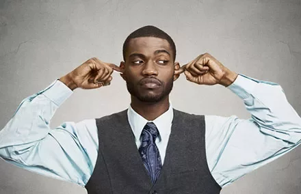 Man in vest and tie closes ears with fingers, looking to the side.