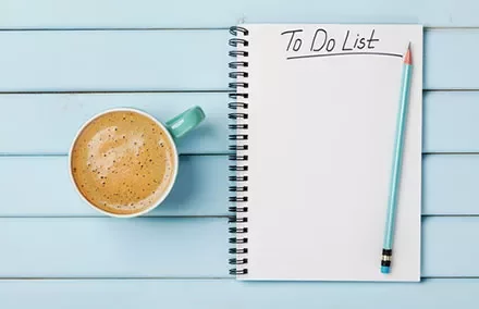 A notepad with 'To Do List' written on it, next to a cup of coffee and a pencil on a blue wooden table.