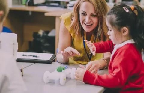 Teacher assisting a child with a toy car in a classroom setting.