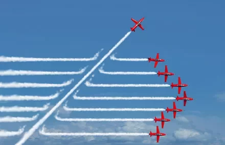 Nine red airplanes, one flying upward, leaving smoke trails in a clear blue sky.