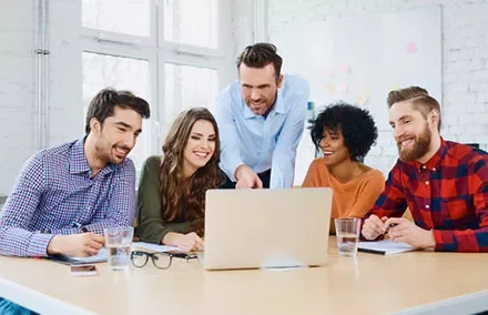 Group of coworkers smiling and collaborating around a laptop in a bright office.