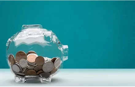 Clear piggy bank filled with various coins against a teal background.