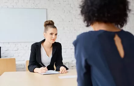 Two women in a professional interview setting, one writing notes.