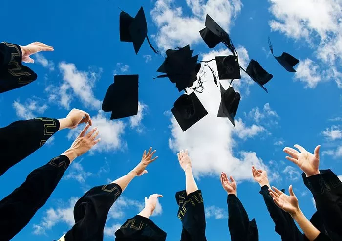 Graduates throwing caps in the air against a blue sky with clouds.