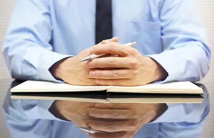 Person in a blue shirt sitting at a desk with a notebook and pen.