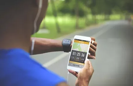 Person running with fitness tracker and smartphone, tracking activity data.