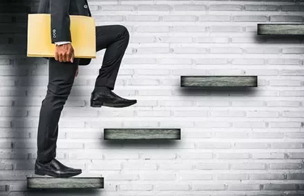 Businessman ascending steps with briefcase against a brick wall.