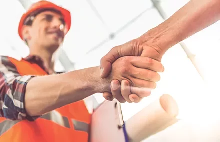 Construction worker in orange vest shaking hands with another person.