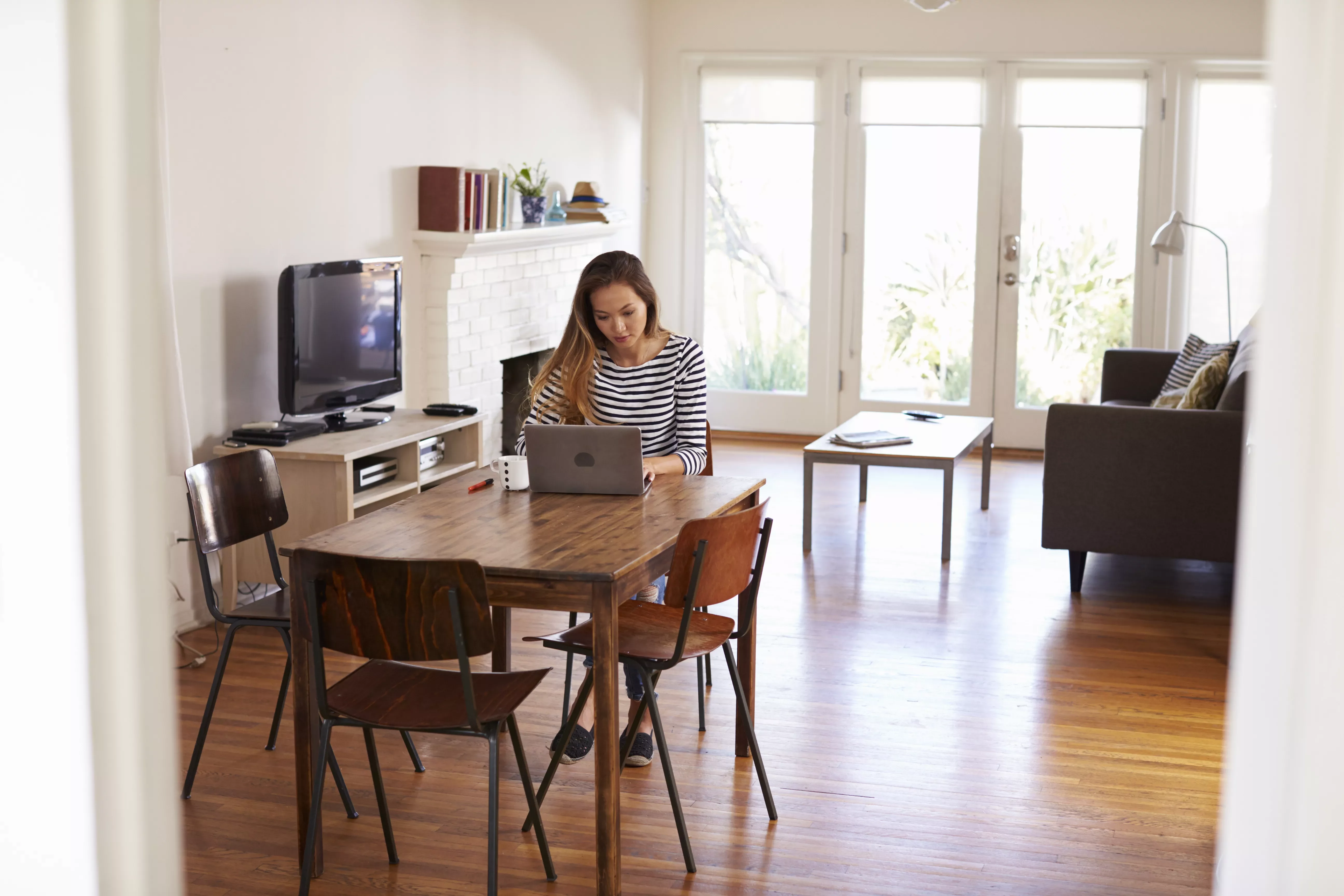 Person working on a laptop at a dining table in a cozy living room.