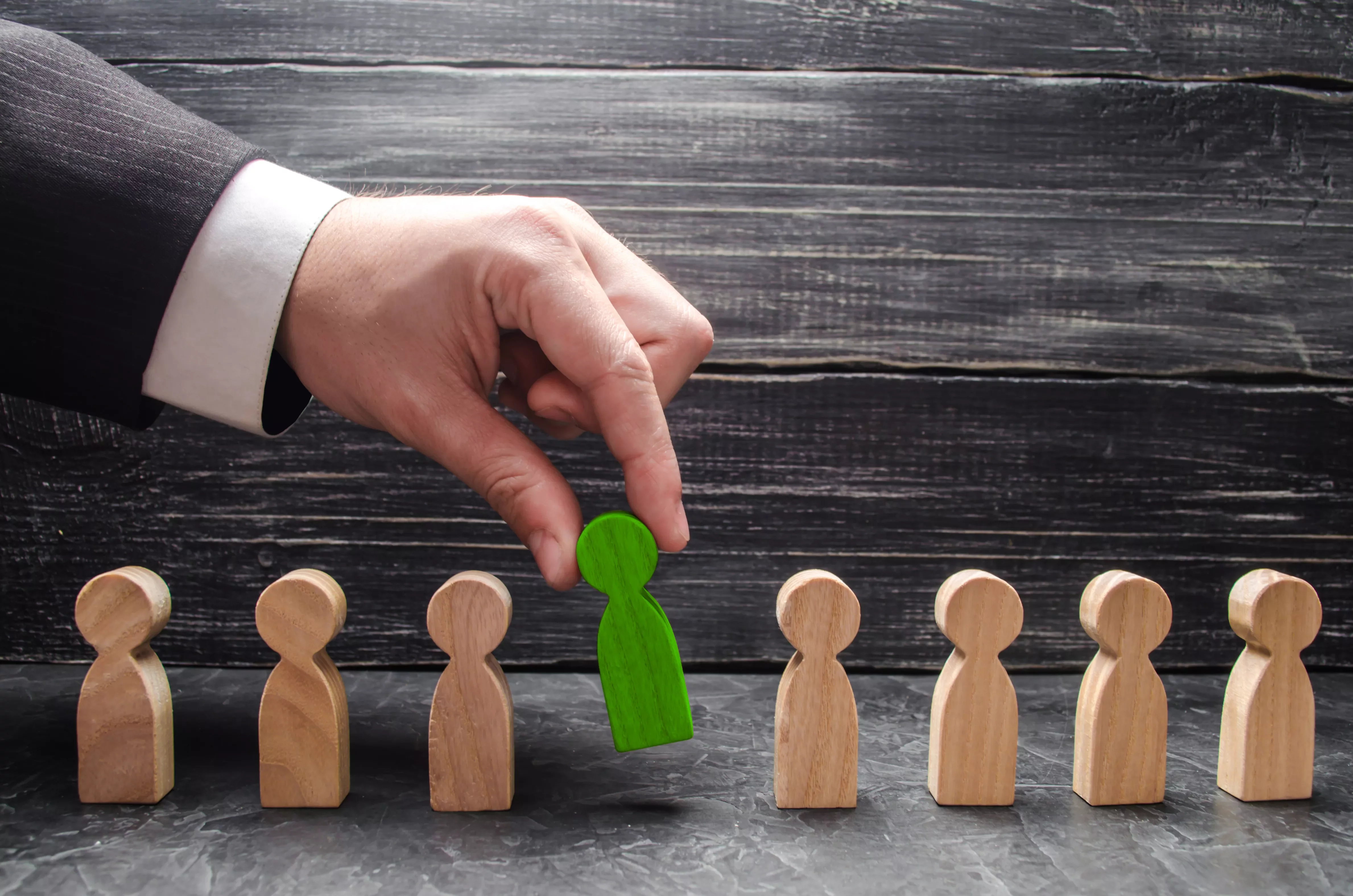 Hand selecting a green wooden figure from a row of plain wooden figures.