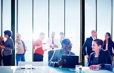 Colleagues mingling and discussing in a modern office with large windows.