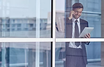 Businessman talking on phone and using a tablet by a window.