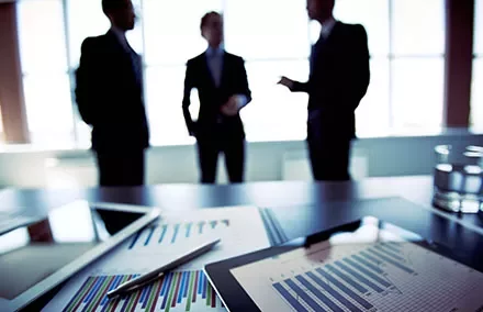 Three businesspeople discussing in an office with documents and charts on the table.