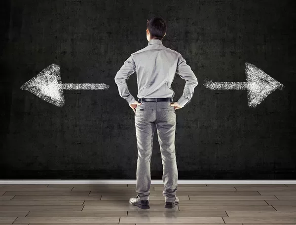 Back view of man facing two chalk-drawn arrows on a blackboard, one pointing left and the other right.