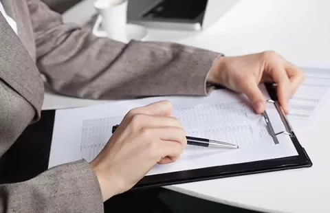 Person in suit reviewing documents on clipboard at desk.