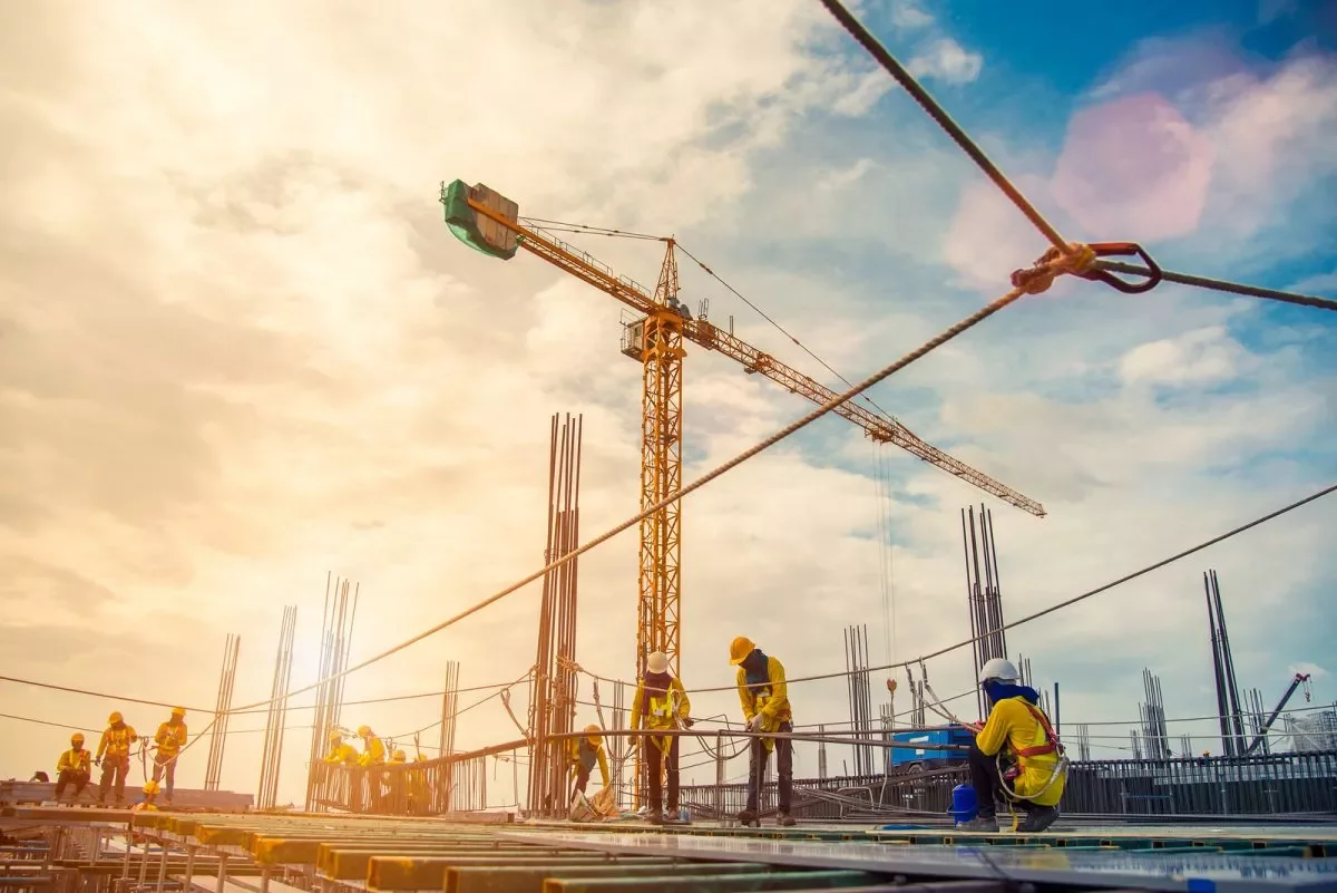 Construction workers on a building site with cranes and scaffolding under a bright sky