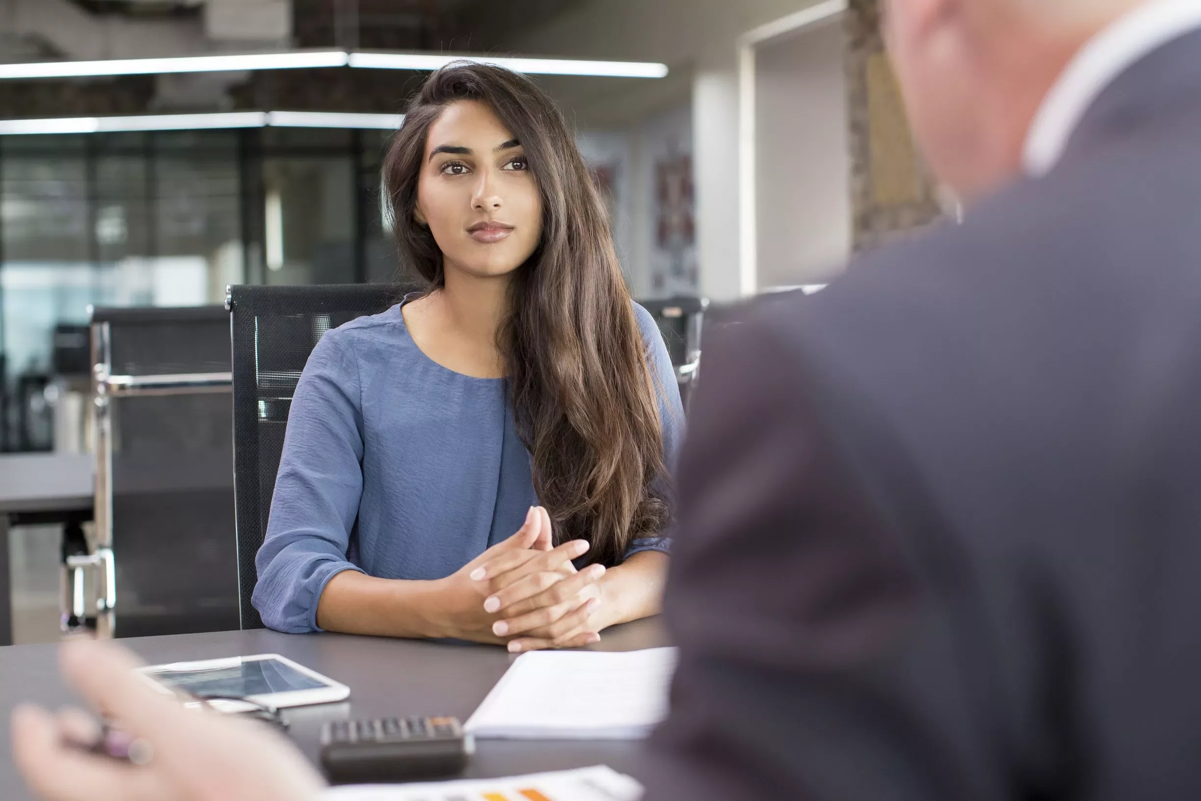 Woman in blue shirt sitting at a desk during a meeting.