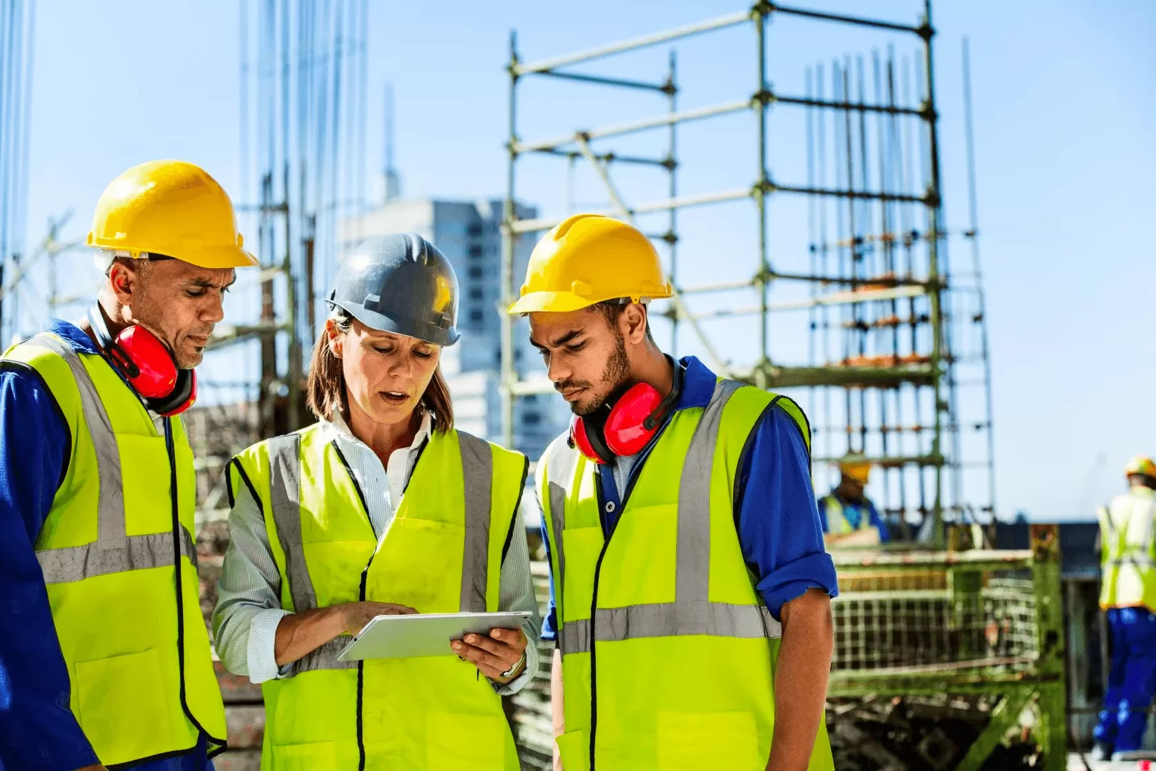 Three construction workers wearing safety gear discussing a project on site.