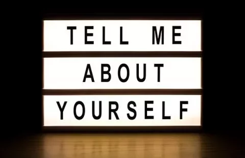 Lit sign displaying the phrase 'Tell me about yourself.'