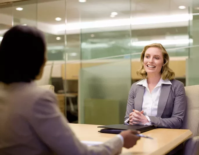 Two people in a business meeting, smiling and talking across a table.