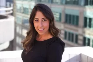 Woman with long hair smiling on a rooftop with a city building in the background.