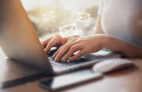 Hands typing on a laptop with floating email icons.