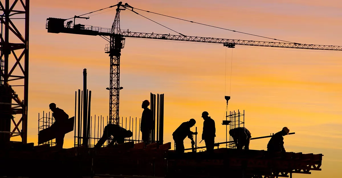 Silhouettes of construction workers and a crane at sunset.