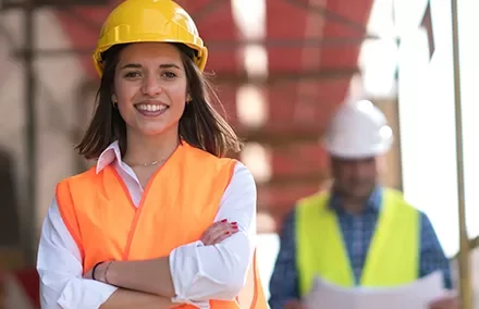 Smiling woman in a construction helmet and safety vest, standing confidently.
