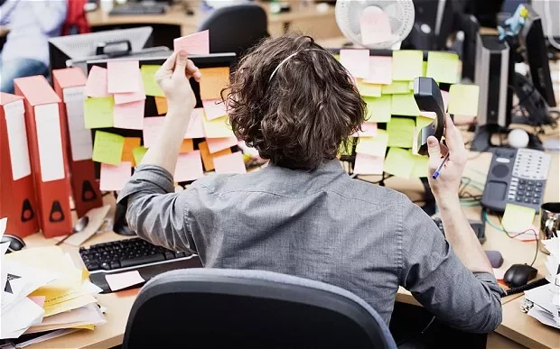 Person at desk surrounded by sticky notes and binders, holding a phone.