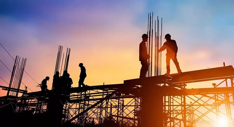 Silhouetted construction workers on scaffolding at sunset