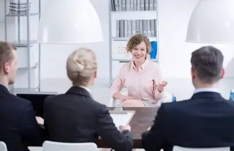 Woman smiling during a job interview with a panel of interviewers in an office.